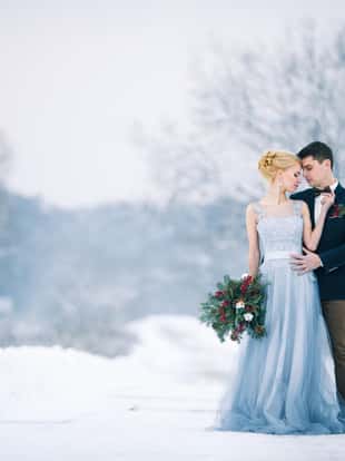 Bride and groom among snowy landscape. Bride and groom are standing and hugging.  Winter wedding outdoors. Copy space.