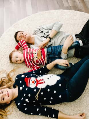 Flat lay, top view. Happy family: mom, dad and little son in Santa Claus sweaters, lying down on floor. Enjoying love hugs, holidays people. Togetherness concept. Merry Christmas and Happy New year.