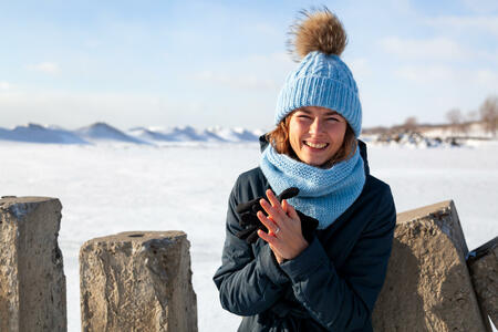Portrait beauty woman model on winter background. Beautiful modern urban young woman wearing blue knitting hat  basks in cold weather on the background of the frozen sea