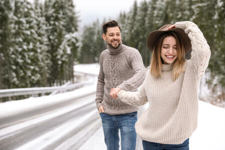 Couple walking near snowy forest, space for text. Winter vacation
