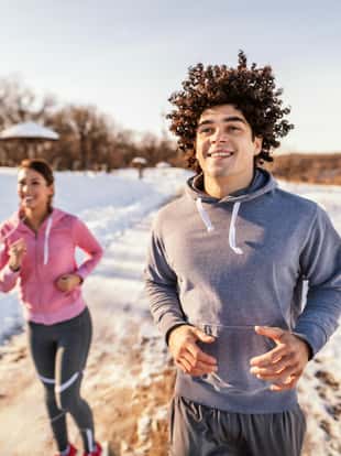 Happy caucasian couple wearing sportswear and running on the trail in nature. Winter fitness concept.
