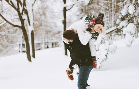 A pretty couple, boy and girl, having fun in snow, he lift up his girlfriend on shoulder