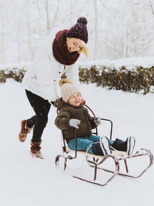 Photo of handsome mother pushing his son in sladge in winter park,  having fun putside.