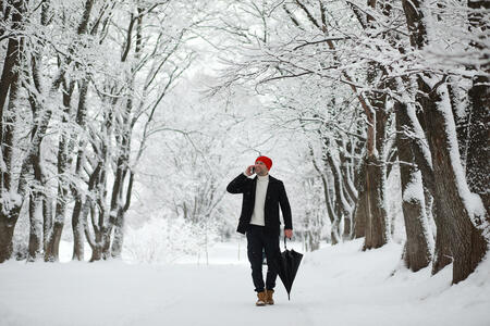 A man on a walk in the park. Young man with an umbrella under the winter snowfall.