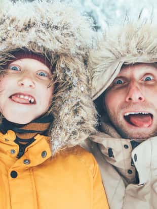 Father and son fooling into the camera. They showing their tongues and making grimaces. Parent and children winter holidays spending concept image.