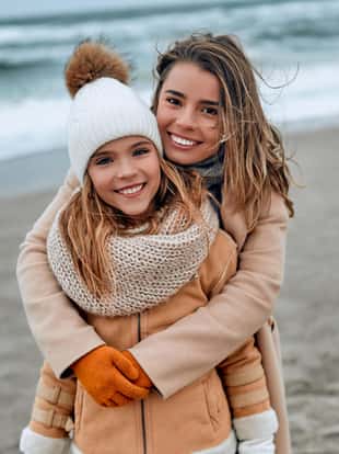 Portrait of a beautiful young mother in a coat with her cute daughter in a knitted hat on the beach in winter.
