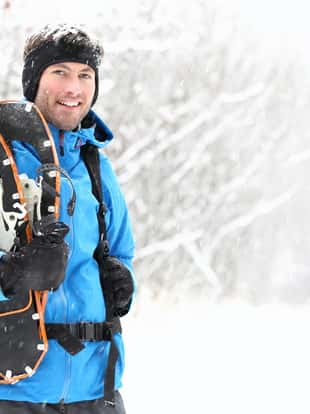 Winter snowshoeing. Young outdoorsman hiker standing smiling happy holding snowshoes outside in the snow during snowshoe hiking trip. From Quebec, Canada.