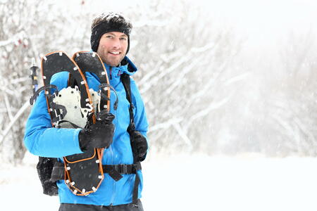 Winter snowshoeing. Young outdoorsman hiker standing smiling happy holding snowshoes outside in the snow during snowshoe hiking trip. From Quebec, Canada.