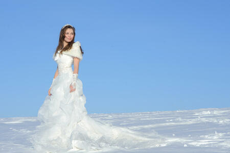 pretty young woman posing in wedding dress with train, on winter snow