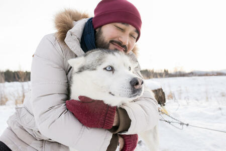 Portrait of bearded Asian man hugging gorgeous husky dog enjoying nice wither day on walk in the woods, copy space