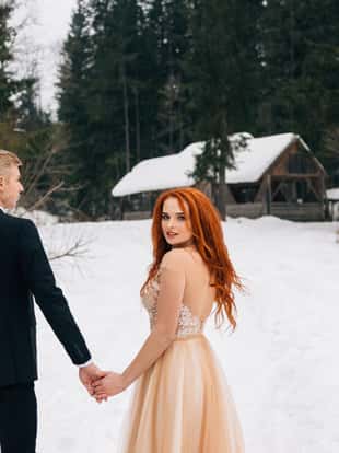 Beautiful red-haired girl in winter dress holding a guy's hand. Bride and groom, wedding in the winter. Place for text.
