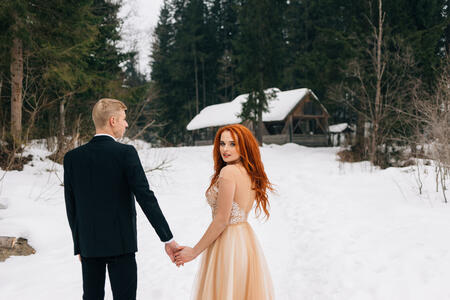 Beautiful red-haired girl in winter dress holding a guy's hand. Bride and groom, wedding in the winter. Place for text.