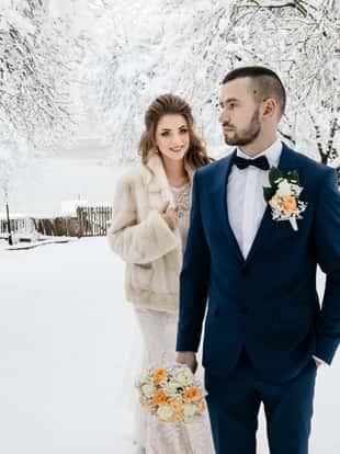 Wedding couple, bride and groom in winter holding hands together over snowy forest background