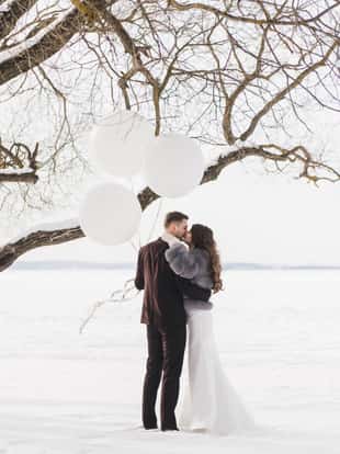 Bride and groom among snowy landscape with big white balloons. Bride and groom walk the snowy road. Beautiful winter fairy tale, wedding card