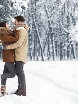 Christmas Romance. Loving Couple Embracing Standing In Snowy Winter Forest Or Park In The Morning. Empty Space For Text