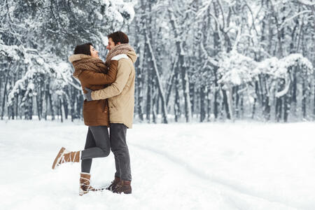 Christmas Romance. Loving Couple Embracing Standing In Snowy Winter Forest Or Park In The Morning. Empty Space For Text