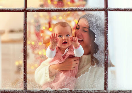 cute infant baby girl in mother hand looking through the window, family winter holidays