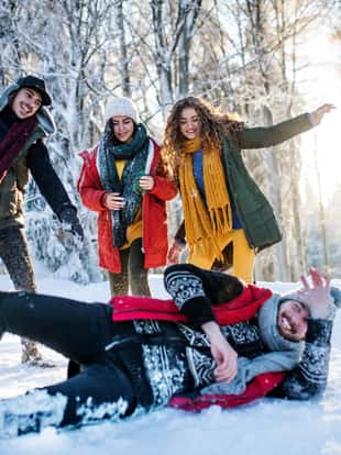 A group of young cheerful friends on a walk outdoors in snow in winter forest, having fun.