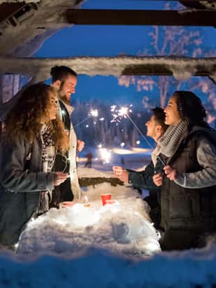 A group of young friends outdoors in snow in winter at night, holding sparklers.