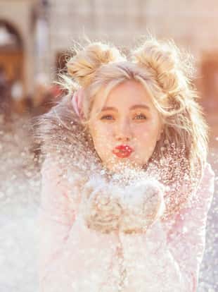 Happy woman blowing snow outdoors in sunny winter city. Girl having fun in the street.
