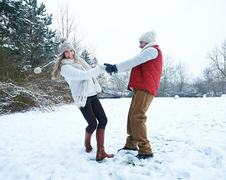 Lachendes Paar tanzt gemeinsam im Schnee im Winter