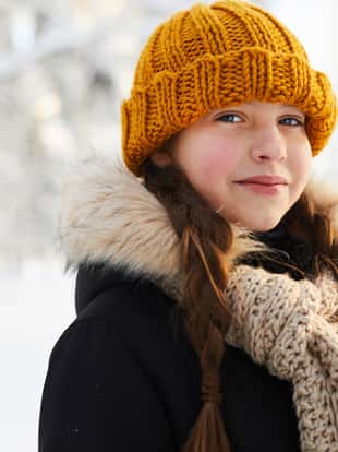 Head and shoulders portrait of smiling teenage girl in winter forest looking at camera, copy space