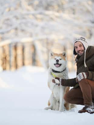 Full length portrait of mature man posing with dog in beautiful winter park, copy space
