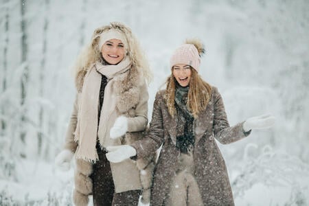 Photo of two blondes throwing snow on walk in winter forest at day