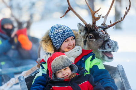 Family of mother and little girl at reindeer safari in winter forest in Lapland Finland