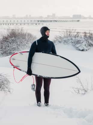 Snowy winter and surfer with surfboard. Winter beach and surfer in wetsuit.