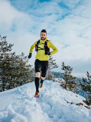 Caucasian man running through the snow covered landscape during the winter.