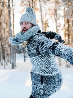 Young man having fun outdoors in winter, jumping in snow.