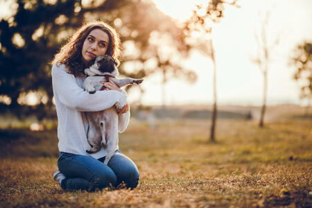 Young female, with curly hair, hugging her dog, pug, in a public park, on a sunny autumn day.