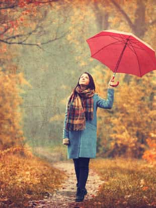 Young beautiful brunette girl in blue coat with umbrella walking in the autumn park