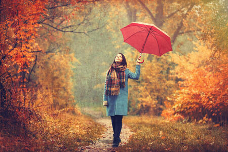 Young beautiful brunette girl in blue coat with umbrella walking in the autumn park