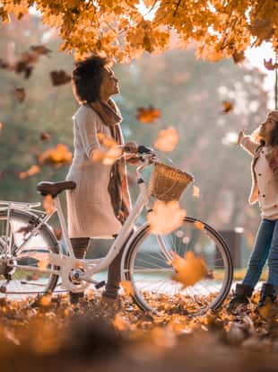 Happy African American mother with a bike enjoying with her daughter in autumn day.