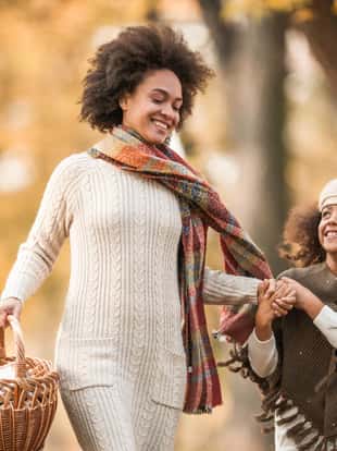 Happy African American mother and daughter running with picnic basket in autumn day at the park.