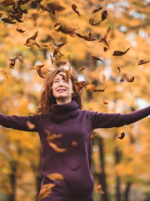 Young happy woman having fun in the park while autumn leaves are falling on her from the tree.