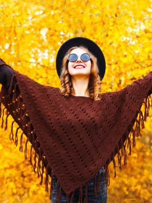 Fashion smiling woman enjoys an autumn park in black round hat, knitted poncho