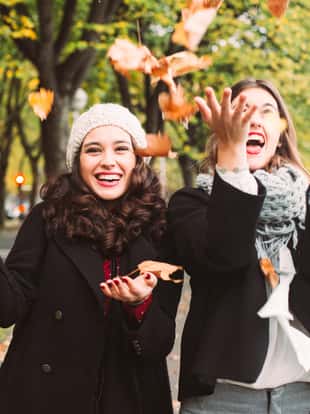 Funny girl friends throwing dry leaves in the city in autumn
