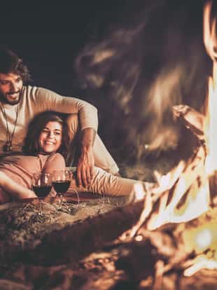 Young happy couple relaxing on the beach by the campfire at night.