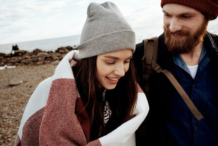 Portrait of young attractive brunette walking with handsome bearded man by the sea on cold autumn afternoon and smiling happily