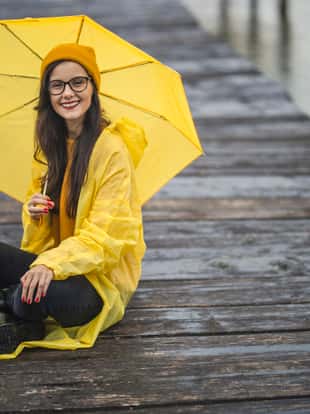 Young woman with yellow umbrella sitting on lake pier