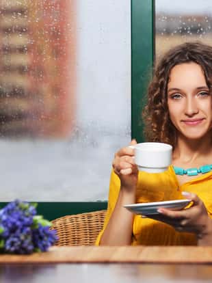 Young fashion woman drinking tea at restaurant Stylish female model with brown curly hairs in yellow shirt