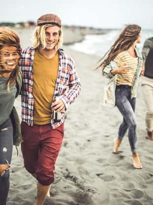 Two happy couples having fun while spending an autumn day on the beach. Focus is on couple in the foreground looking at camera.