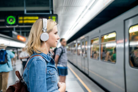 Beautiful young blond woman in denim shirt with earphones, standing at the underground platform, waiting to enter a train