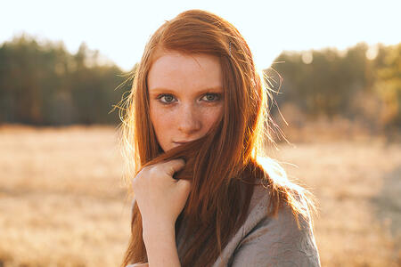 Portrait of Beauty Teenage Model Girl with Red Hair on the Background of Nature on the Field in Sun Light. Face of Young Woman with Freckles. Autumn. Glow Sun, Sunshine. Backlit. Warm Color Tones