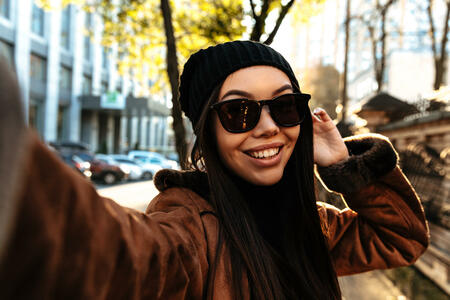 Autumn city walk. Woman portrait. Stylish girl in casual clothes is doing selfie and smiling, outdoors