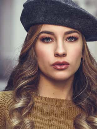 Blonde russian woman in urban background. Beautiful young girl wearing beret, black leather jacket and mini skirt standing in the street. Pretty female with long wavy hair hairstyle and blue eyes.