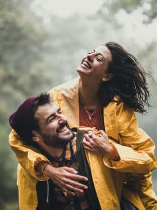 Young cheerful couple having fun while piggybacking during bad weather conditions in nature.